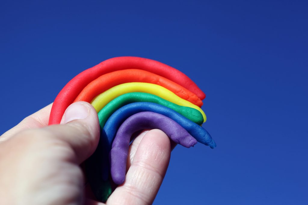 Creative play with rainbow-colored clay held against a vivid blue sky, symbolizing diversity and freedom.